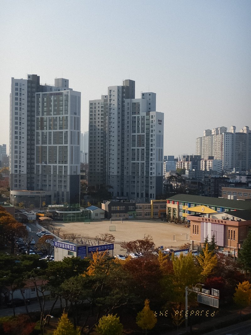 고층 아파트 단지와 학교 운동장이 보이는 탁 트인 도시 풍경 사진입니다.