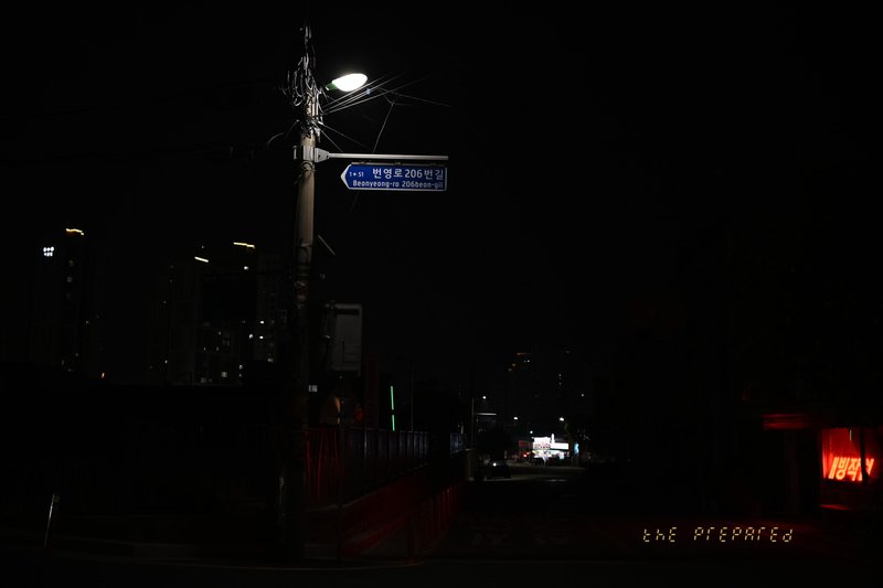 검은 배경에 파란색 거리 표지판과 희미한 가로등 불빛이 보이는 밤거리 사진.