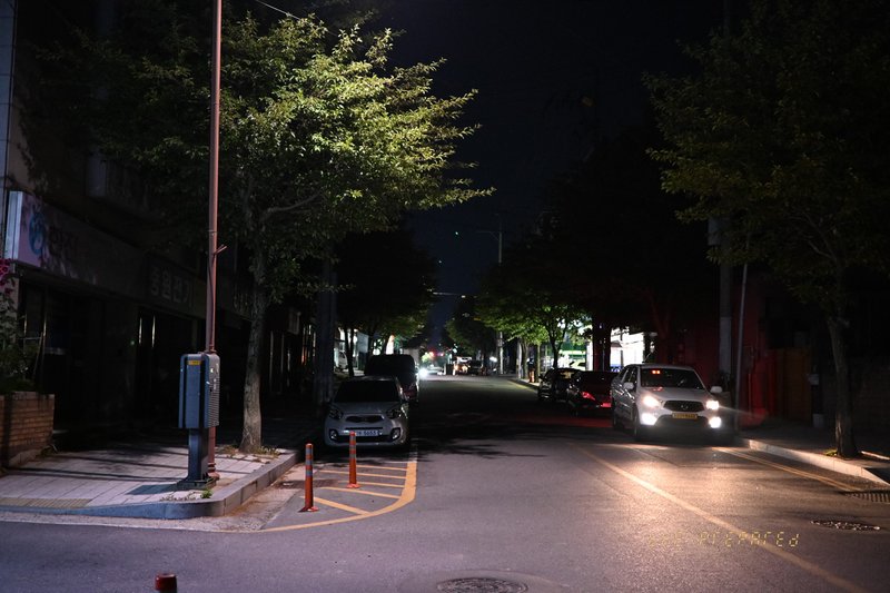가로등 불빛이 희미하게 거리를 비추는 어두운 밤, 자동차 몇 대가 주차된 한적한 골목길 풍경 사진입니다.