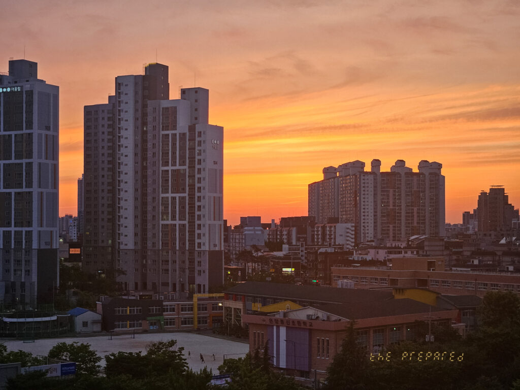 붉은 노을이 하늘을 가득 채운 도시 풍경 이미지. 이미지에는 석양을 배경으로 고층 건물 여러 채가 보입니다.