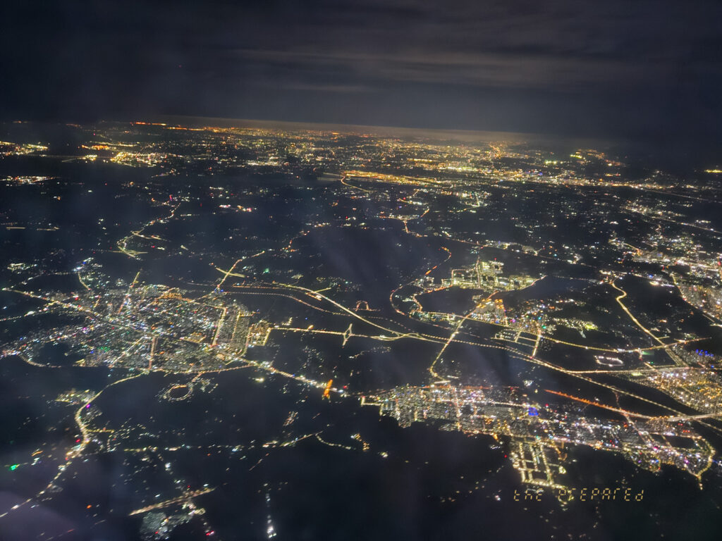 어두운 밤에 하늘에서 찍은 도시의 항공 사진입니다. 사진은 아래 도시의 불빛, 도로 및 건물을 보여줍니다.