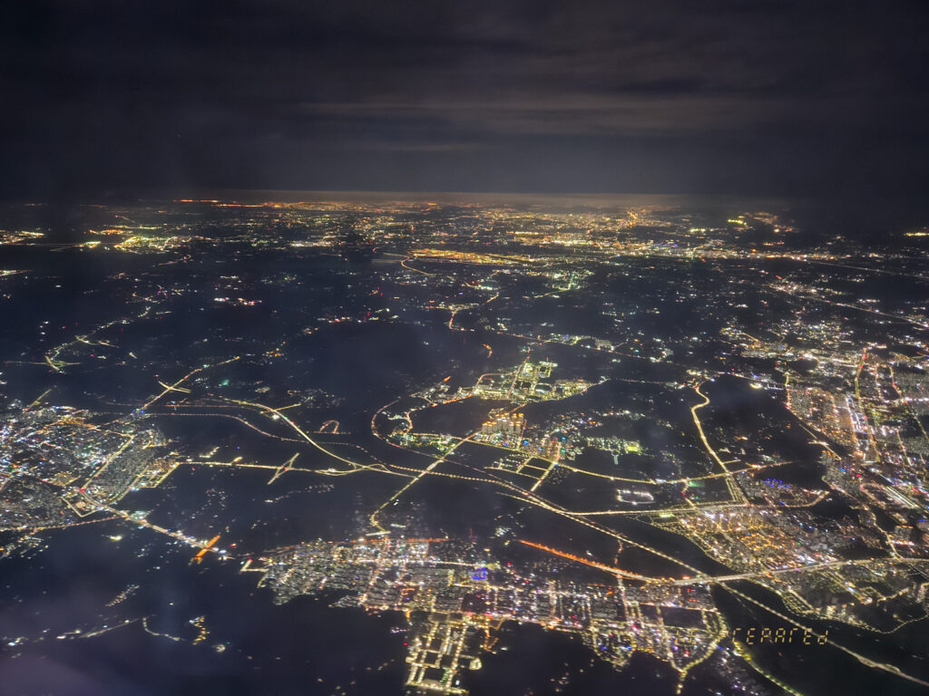 어두운 밤에 하늘에서 찍은 도시의 항공 사진입니다. 사진은 아래 도시의 불빛, 도로 및 건물을 보여줍니다.