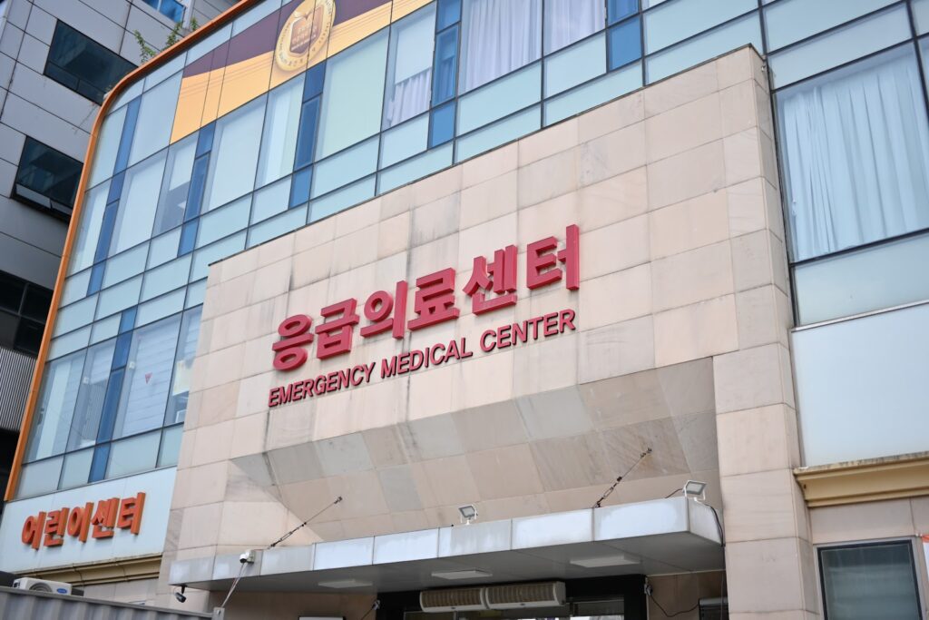 밝은 베이지색 벽돌 외벽에 '응급의료센터'라고 빨간색 글씨가 크게 적혀 있습니다. 건물 모퉁이에는 '어린이 센터'라고 적힌 표지판도 보입니다.