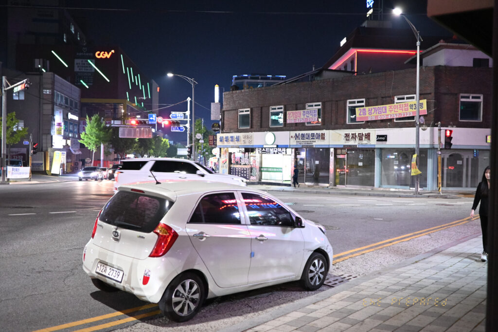 아산시의 밤거리를 담은 사진입니다. 거리에는 자동차와 건물, 신호등이 보이며 오른쪽 건물에 있는 2층 상가 임대 광고판이 눈에 띕니다.