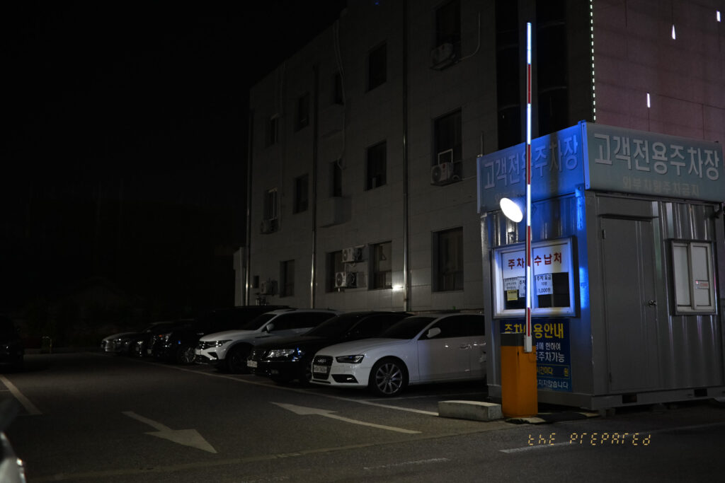 주차된 자동차와 주차장 입구, 고객 전용 주차장 표지판이 보이는 밤 풍경 사진입니다.