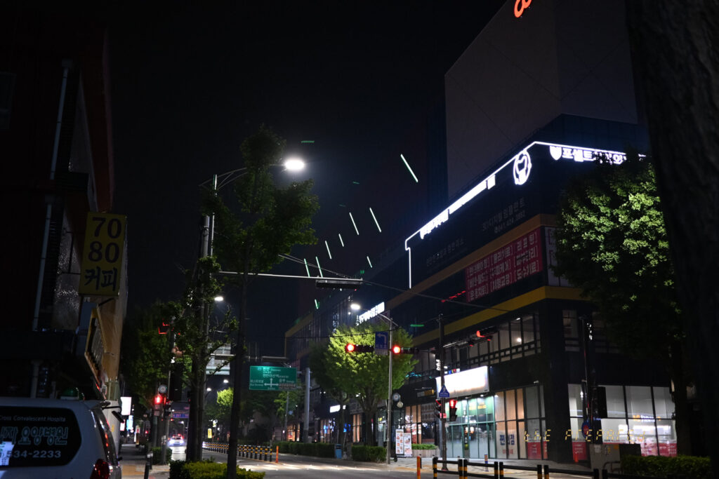 어두운 밤거리에 켜진 가로등과 건물 조명이 대비를 이루며 도시의 밤 풍경을 보여주는 사진입니다.