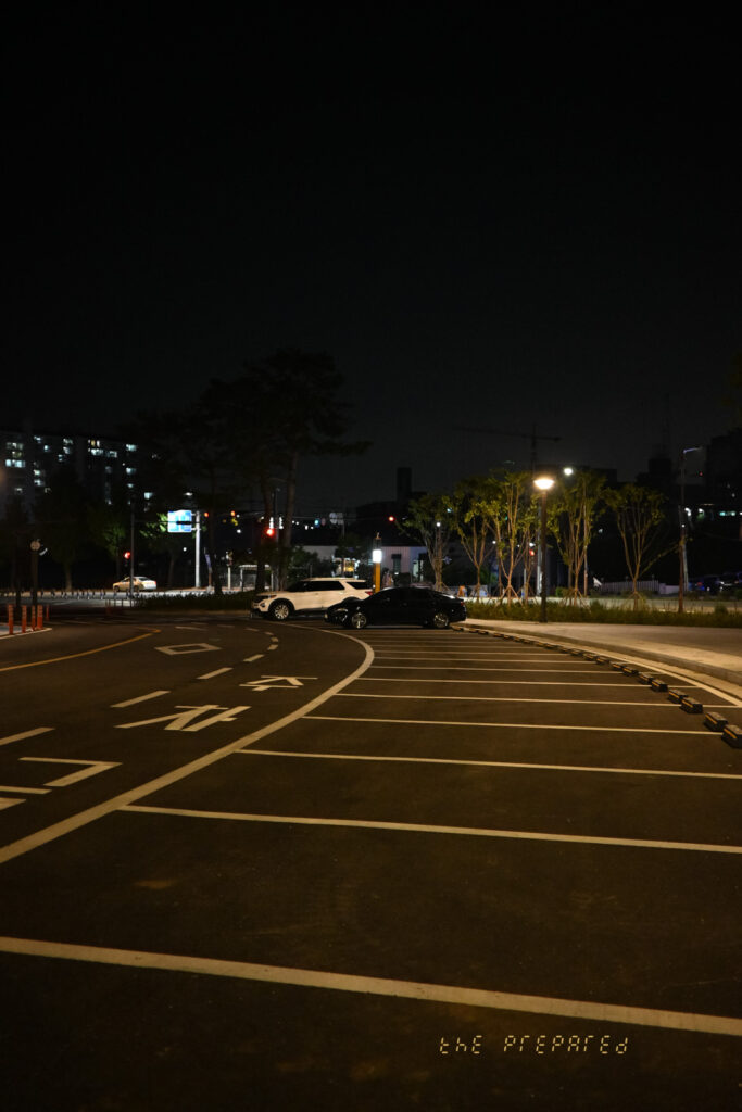 검은 밤에 주차된 두 대의 자동차와 주차장의 도로 사진.