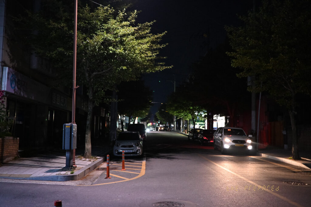 가로등 불빛이 희미하게 거리를 비추는 어두운 밤, 자동차 몇 대가 주차된 한적한 골목길 풍경 사진입니다.