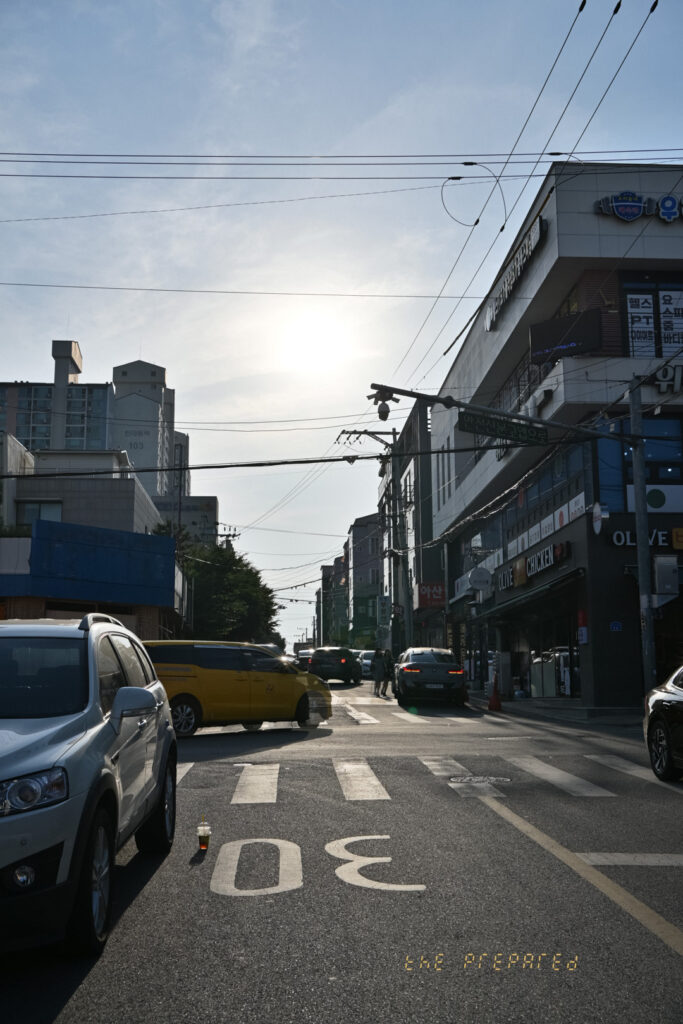 아산시 도시의 거리 사진. 전봇대와 전선이 복잡하게 얽혀 있는 거리의 풍경을 담고 있으며, "30"이라고 적힌 도로 위로 차량들이 지나다니고 있습니다